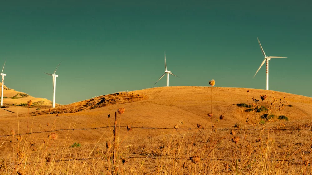 Wind turbines on dry grassy hills under a dramatic cloudy sky.