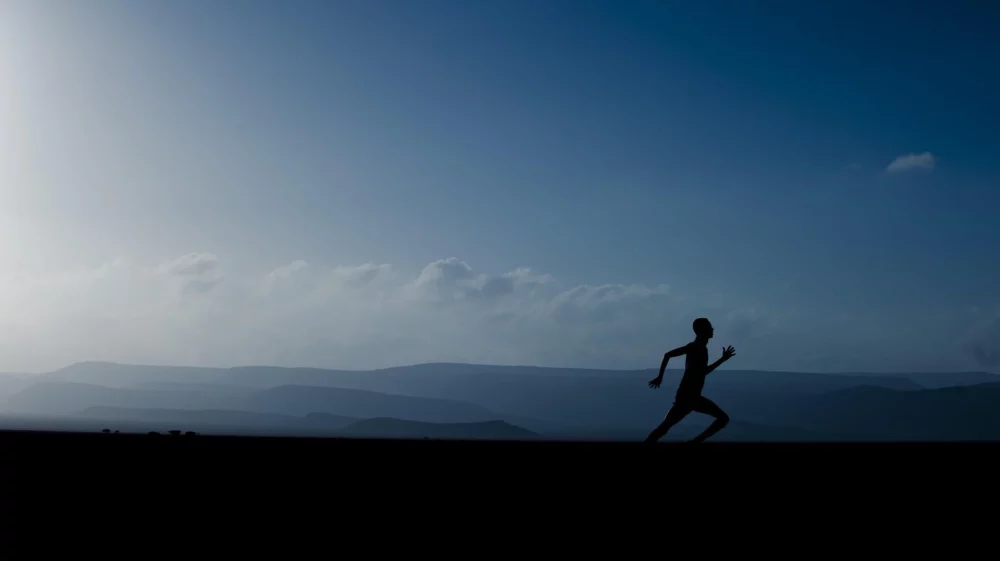 silhouette of an individual running with a backdrop of dark blue sky and mountains