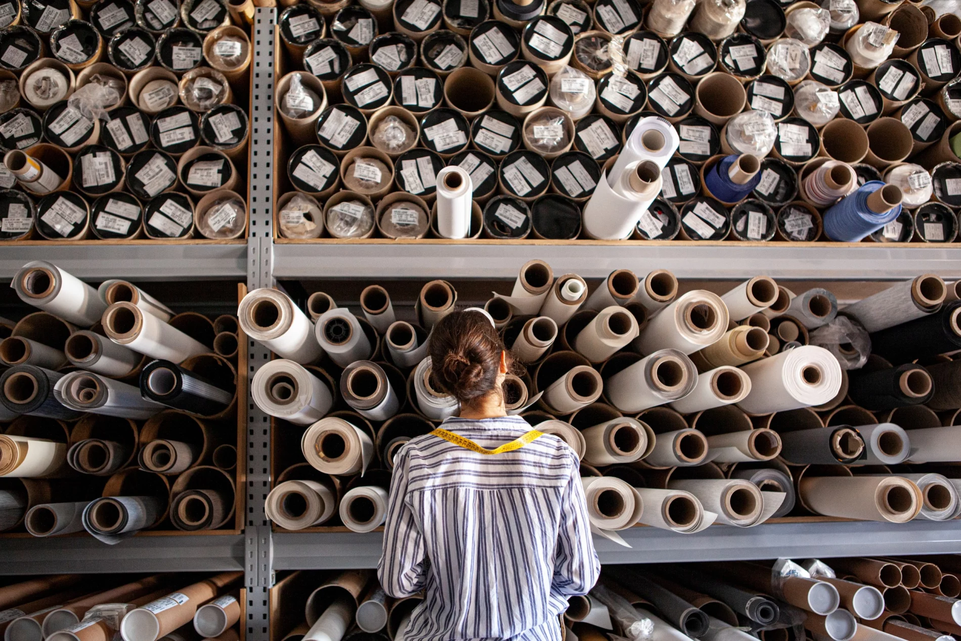 Portrait of textile designer choosing fabric from stack of rolls inside sustainable workshop