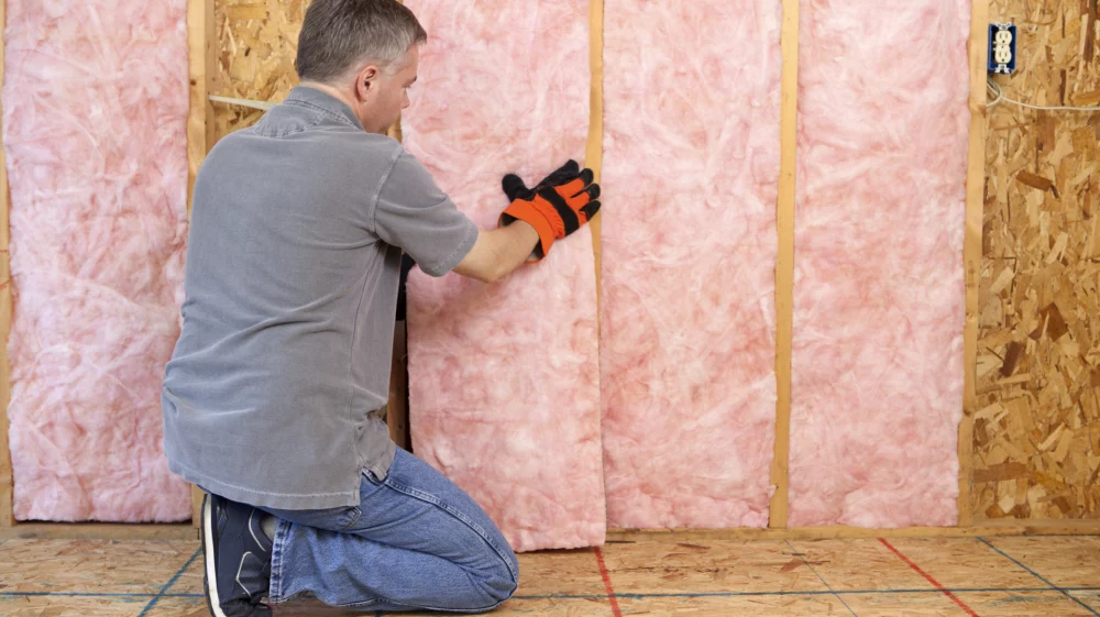 Man sitting on his knee next to a wall, working with insulation