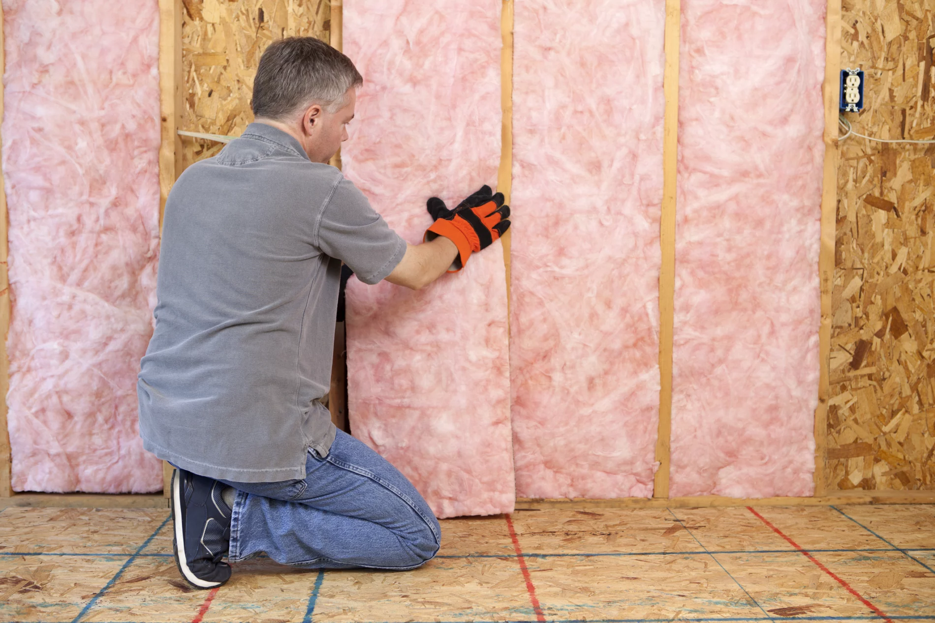 Man sitting on his knee next to a wall, working with insulation