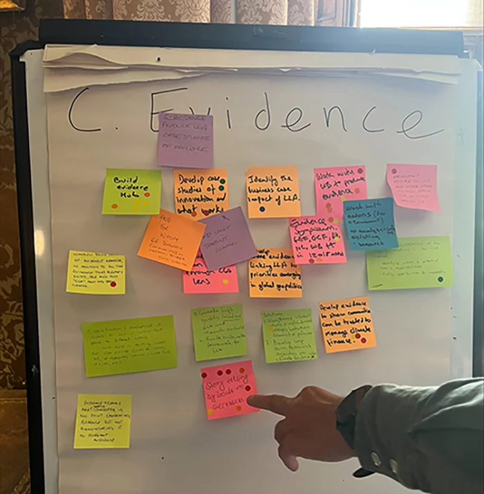 A hand points to a white pad of paper with fluorescent multi-coloured sticky notes with writing -- on top: C: Evidence