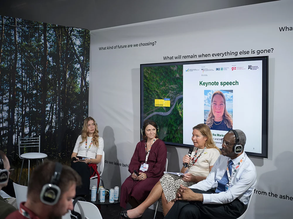 Panel discussion at a conference, with four speakers seated on stage and a keynote presentation displayed on a screen behind them.