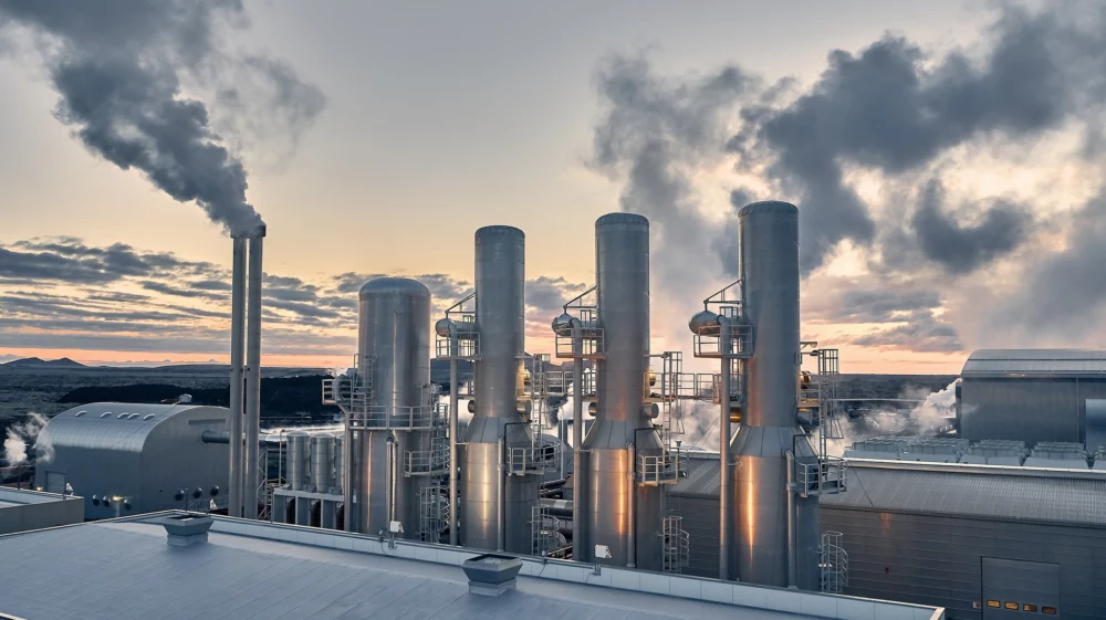 A silhouette of steaming pipes at a geothermal power plant in Iceland release steam into the dusky gray and pink sky.