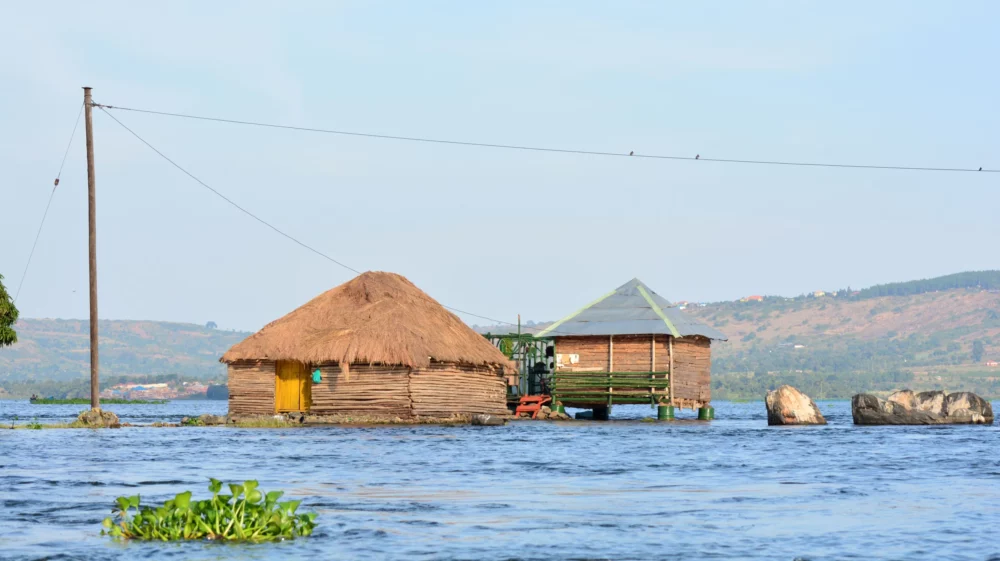 Wooden and thatched huts surrounded by rising water in a lakeside area.