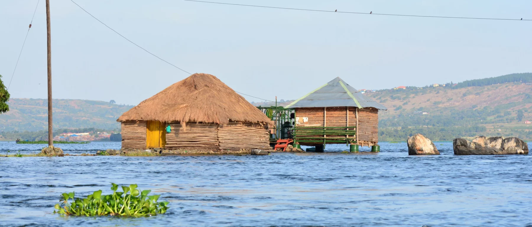 Wooden and thatched huts surrounded by rising water in a lakeside area.
