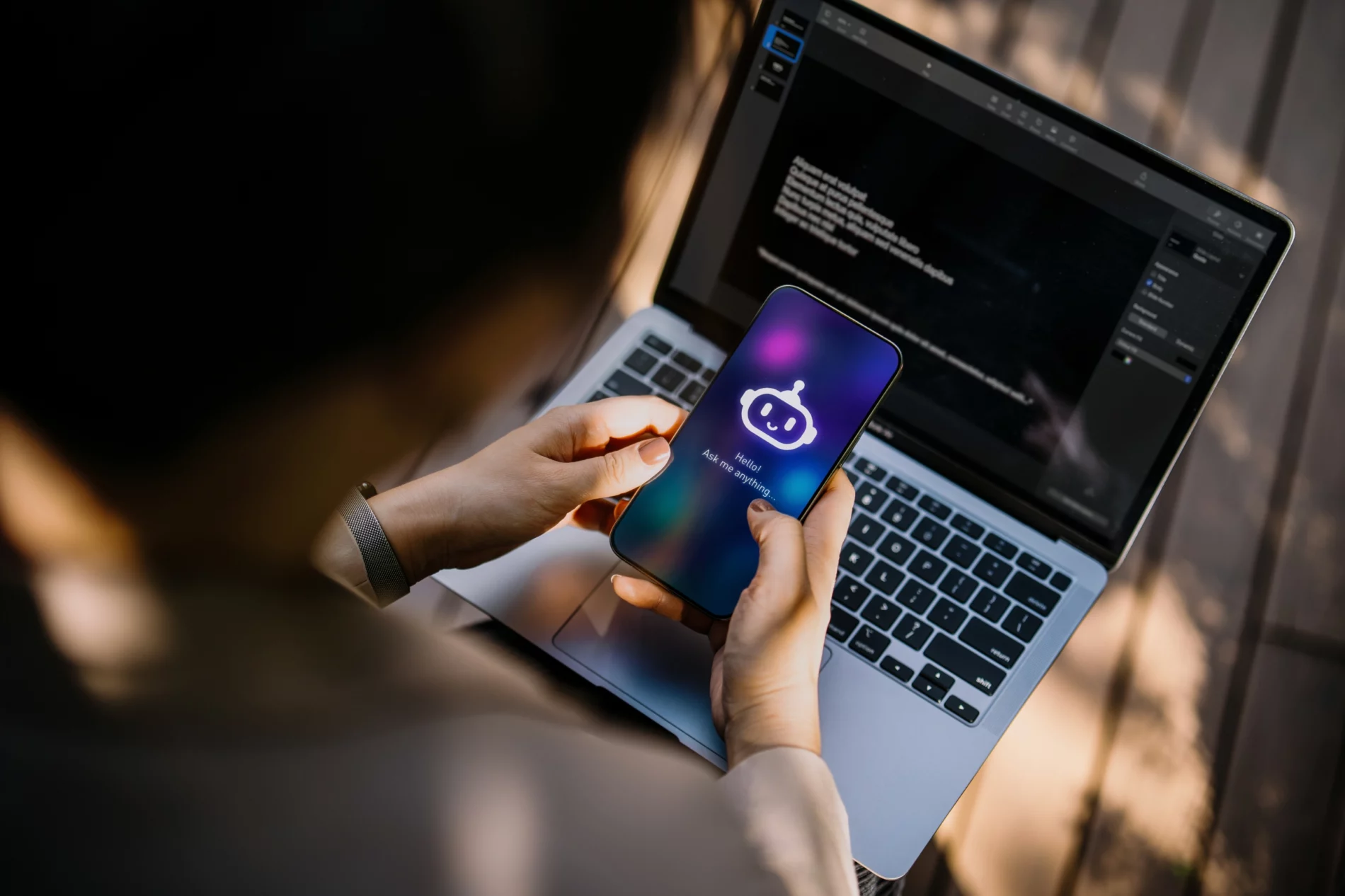 Businesswoman using Chatting AI chatbot virtual assistance app on smartphone to assist her while working on laptop