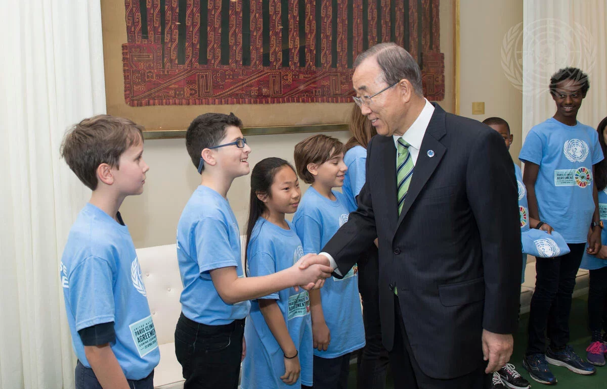 Former UN Secretary-General Ban Ki-moon shakes hands with a student while greeting a line of children wearing light blue UN T-shirts at the signing ceremony for the Paris Agreement.