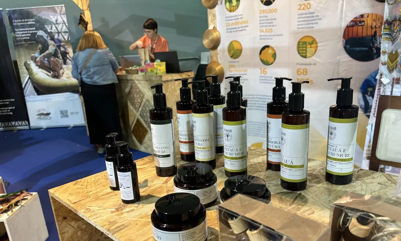 Rows of glass lotion and other dispensers stand on a table with people in the background at a trade conference.