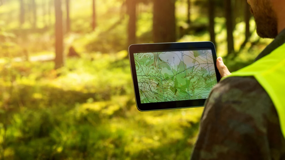 man working with topographic map data on digital tablet in forest. banner with copy space
