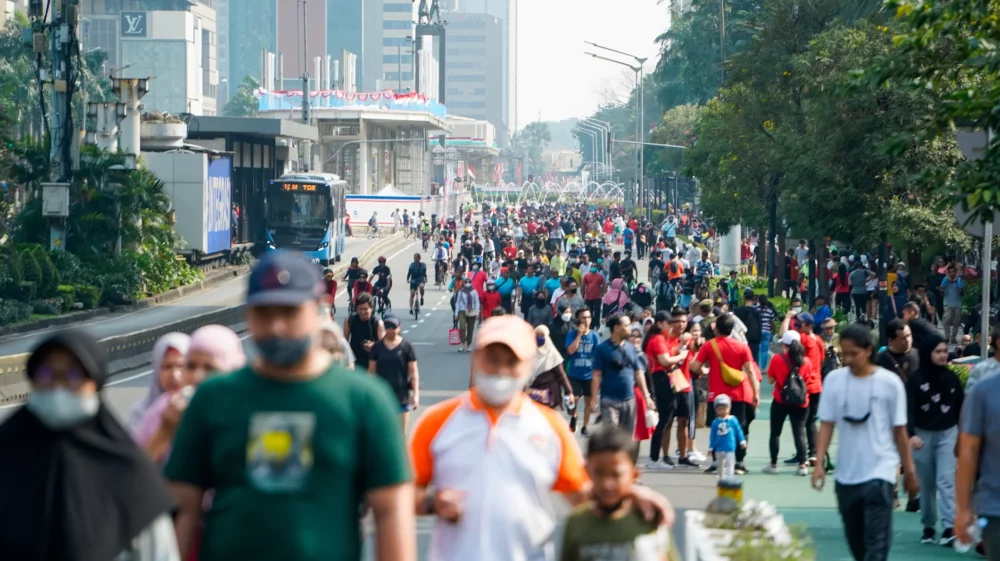 People walking and cycling along a city street in Jakarta.