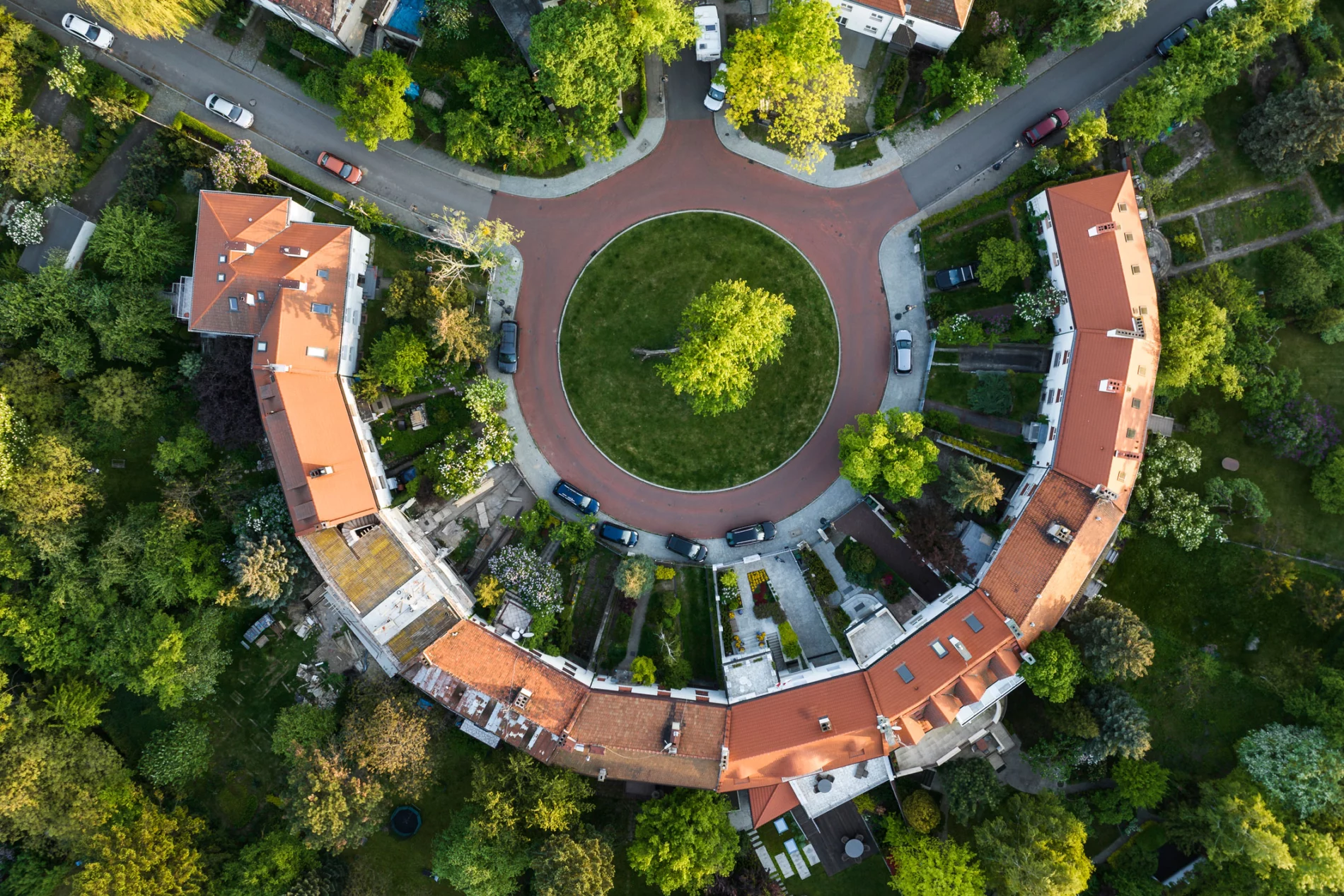 An aerial view of houses arranged in a semi-circle. A green mini-roundabout is at the centre of the images and the tree-covered junction at the top of the image makes the whole thing look slightly like a smiling face.