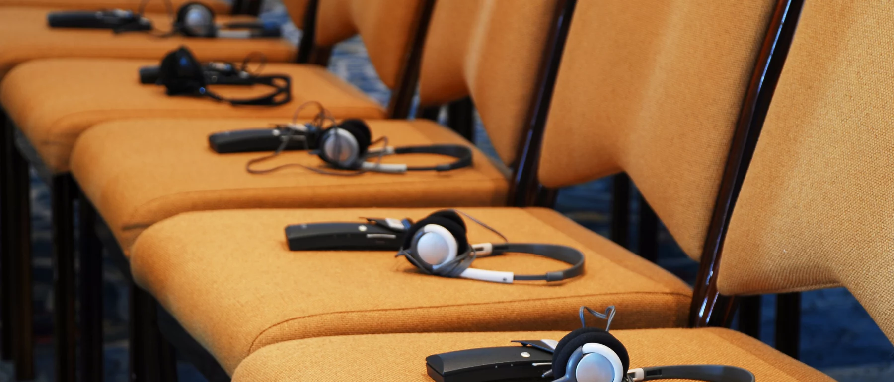 Rows of empty conference chairs with translation headsets placed on the seats.