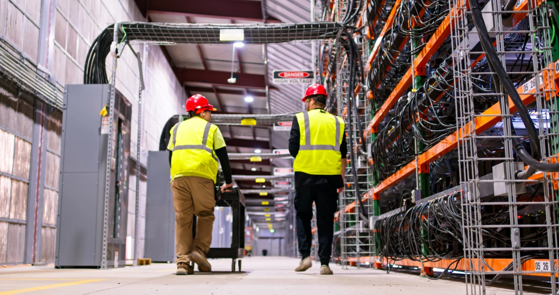 Two technicians wearing PPE walking past racks of equipment in a data center