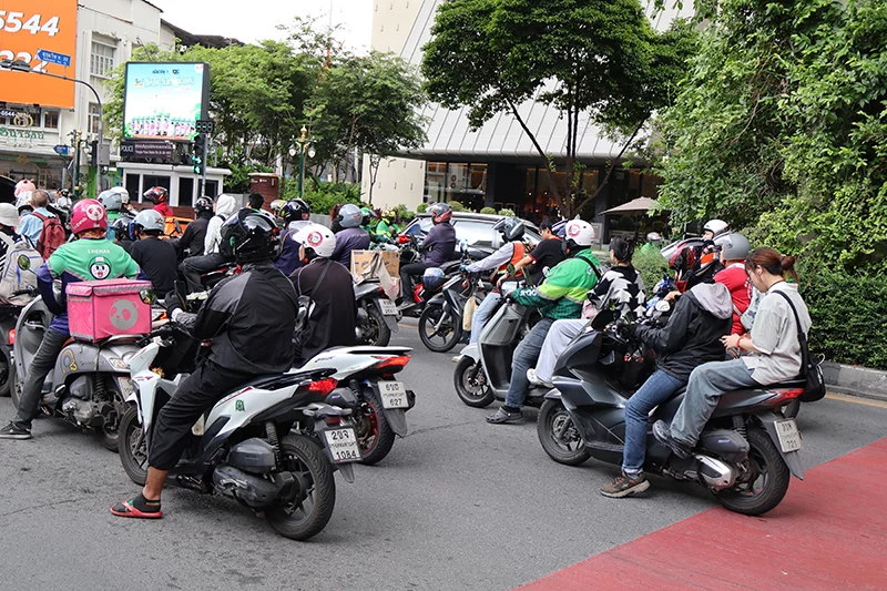 Scooters standing in a traffic jam with several people sitting on most scooters.