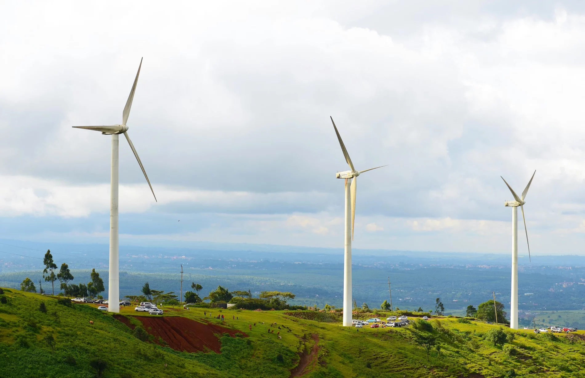 Wind turbines on a green hillside overlooking a wide landscape under cloudy skies.