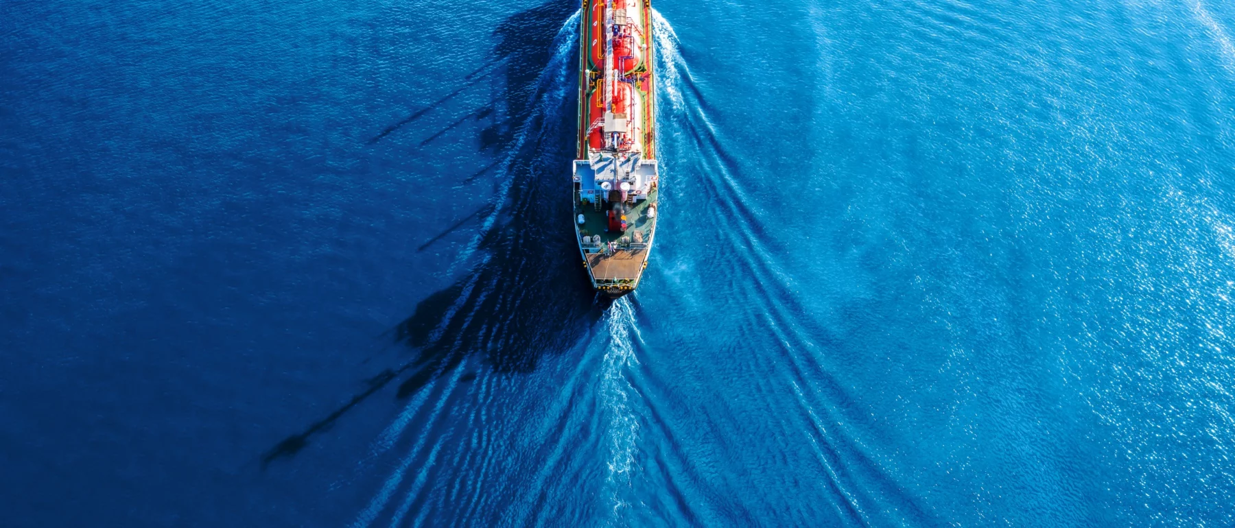 Aerial view of a tanker ship moving across a bright blue sea