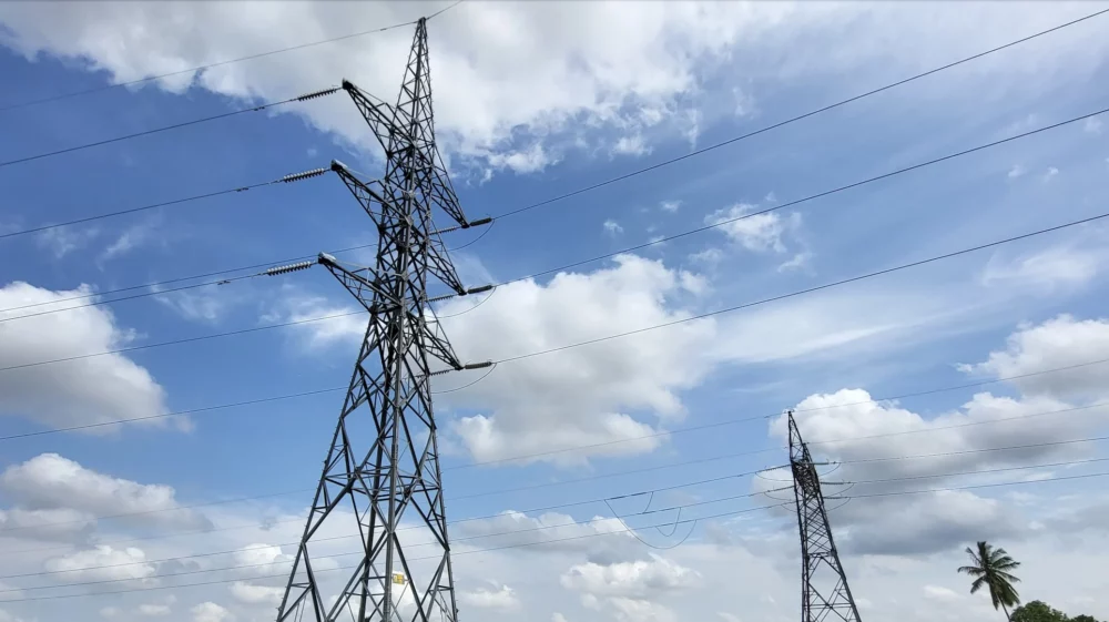 High-voltage transmission towers over grassy rural landscape under blue sky.