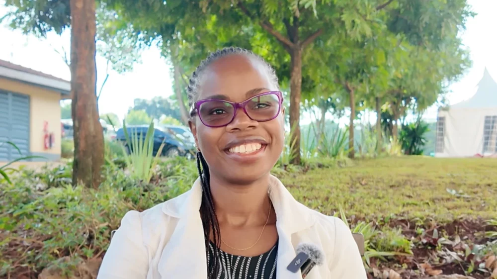 Woman with purple glasses and white jacket smiles in front of trees