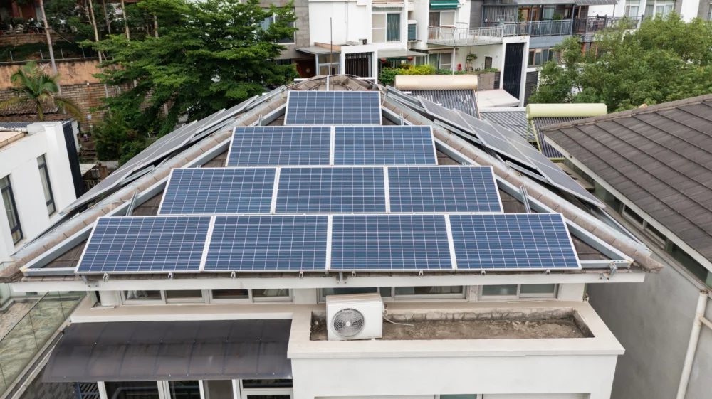 Solar panels mounted across a residential rooftop, with apartment buildings and trees in the background.