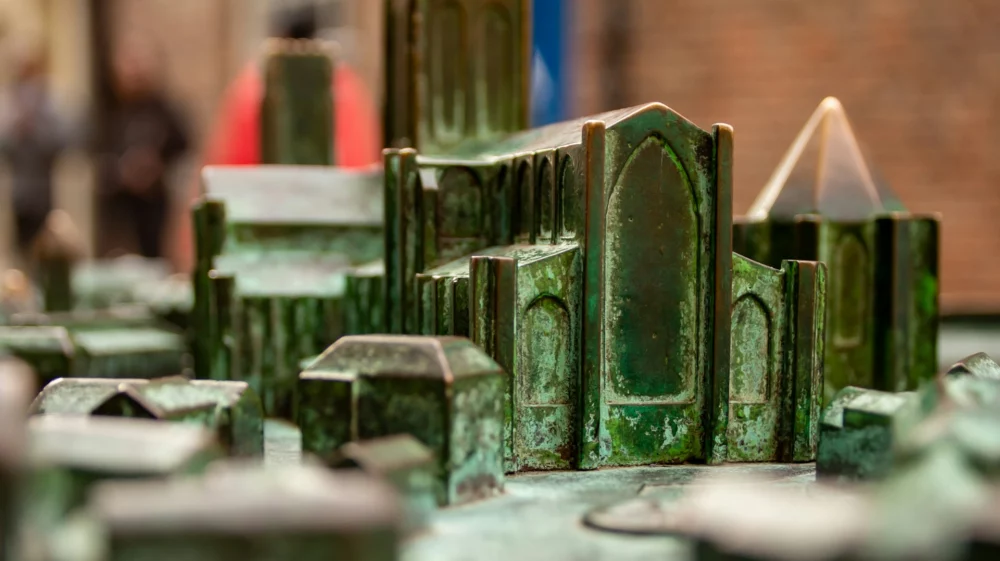 Close-up of a miniature metal model of the York Minster and its outbuildings. The metal has been worn smooth through years of touch, and shines in various colours: greens, dark brassy gold, and coppery orange.