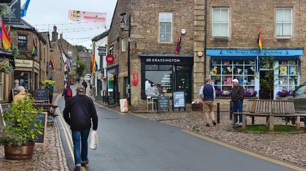 Street scene in North Yorkshire, with stone buildings, shops, benches and rainbow flags.