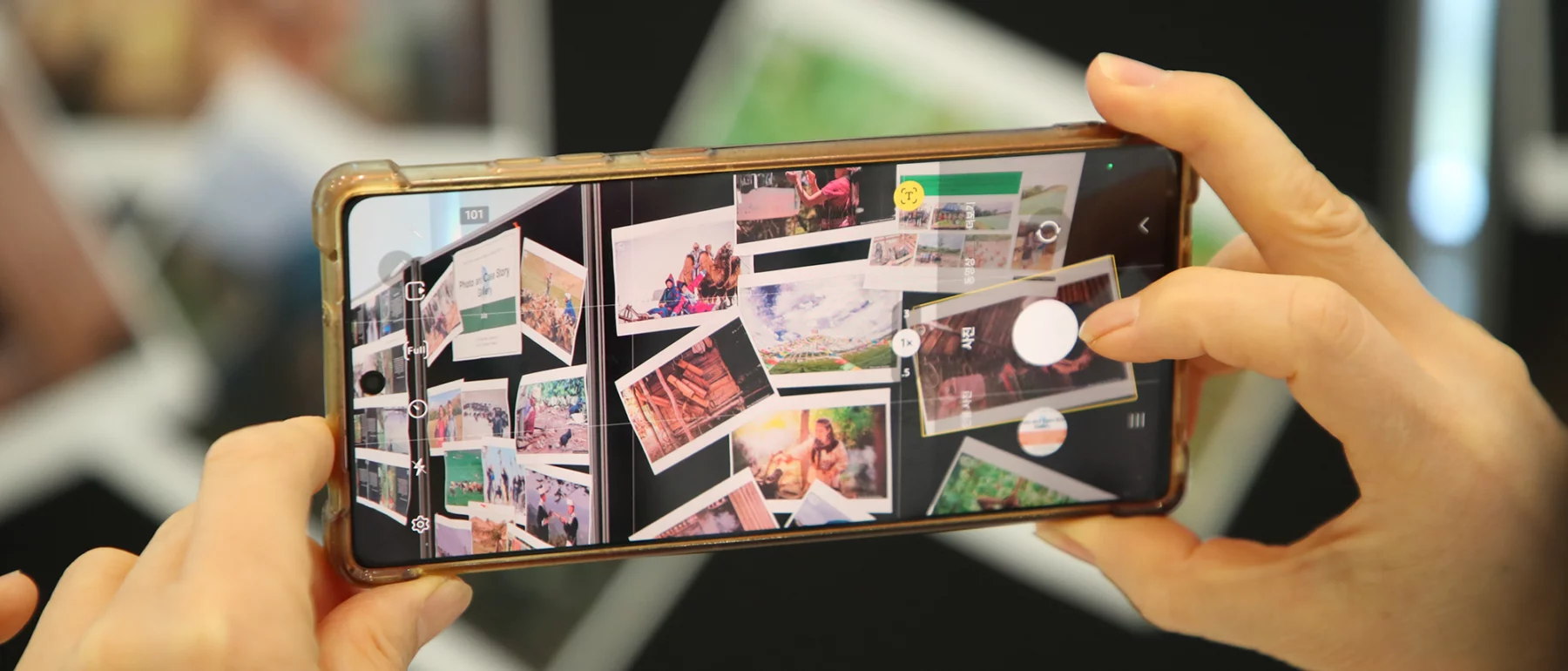Hands holding a smartphone, photographing a scattered pile of printed photos on a table.