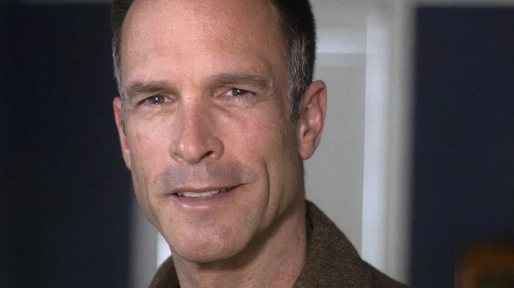 Head shot of Edward R. Carr, wearing a brown blazer over a black shirt, smiling at the camera