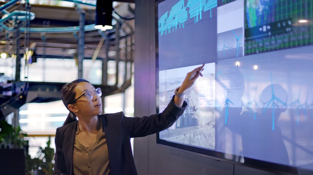 Researcher pointing at a large screen displaying wind turbines, maps and data visualizations.