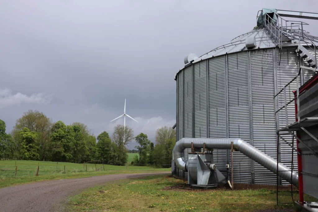 Silo for grain storage and wind mill in background.