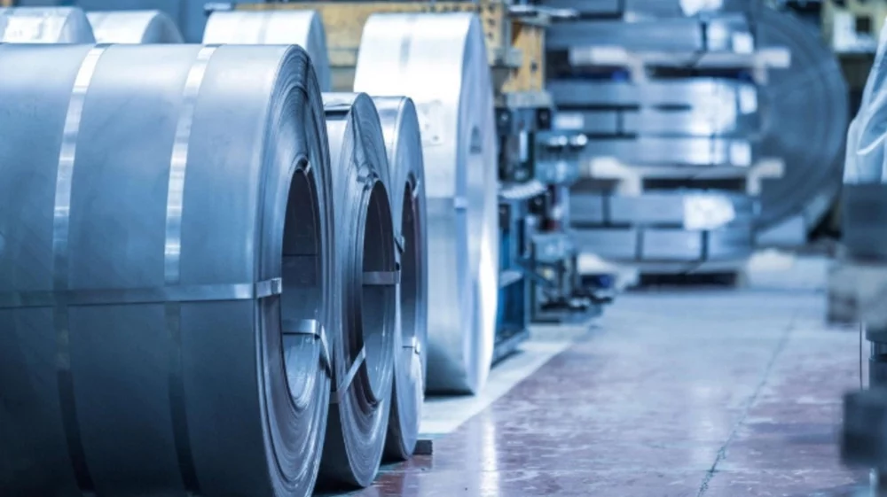 Large steel coils lined up in an industrial facility, with more stacked sheet metal in the background.