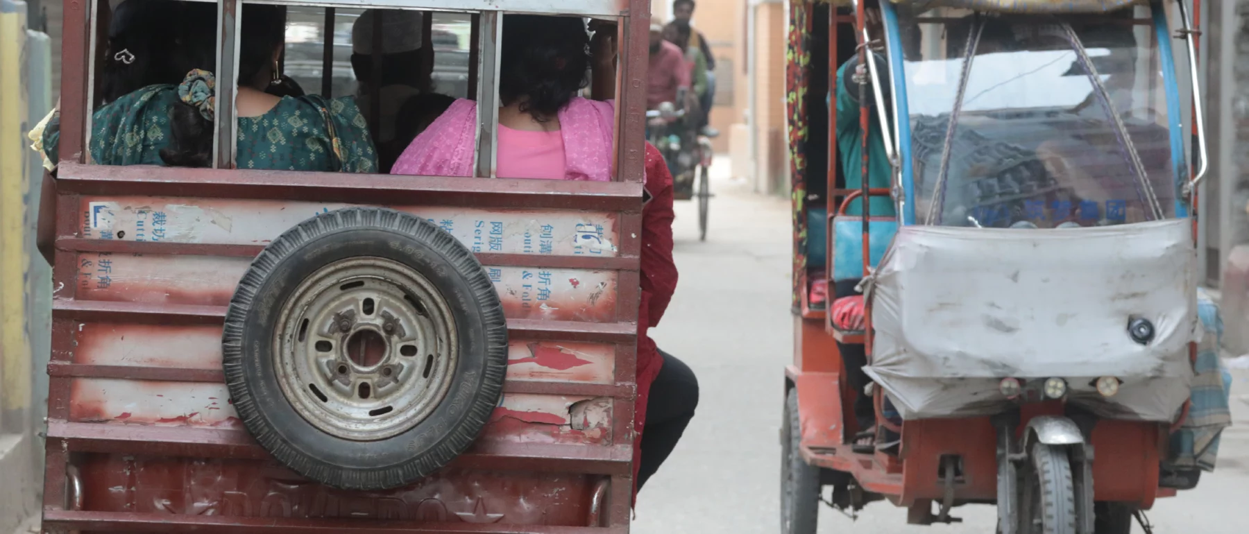 Two three-wheeled tuk tuks, one heading away from the viewer on the left and the other toward the viewer on the right.