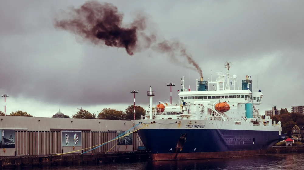 A white and blue docked ship emitting black smoke
