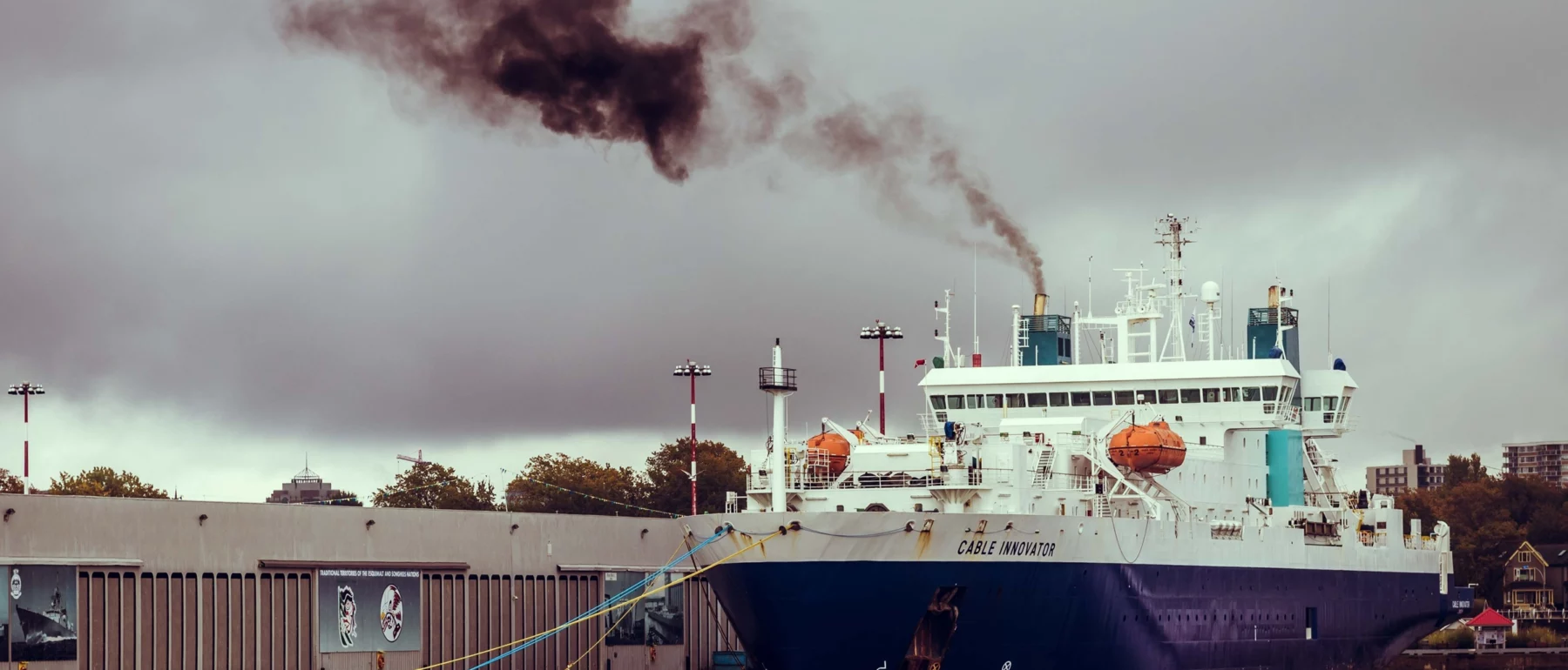 A white and blue docked ship emitting black smoke