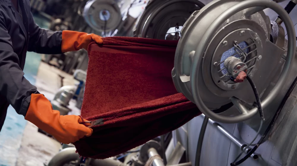 Hands in red gloves holding fabric that comes out from the machine in the factory environment