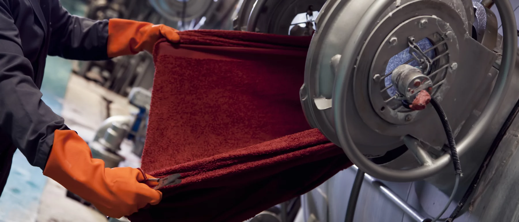 Hands in red gloves holding fabric that comes out from the machine in the factory environment