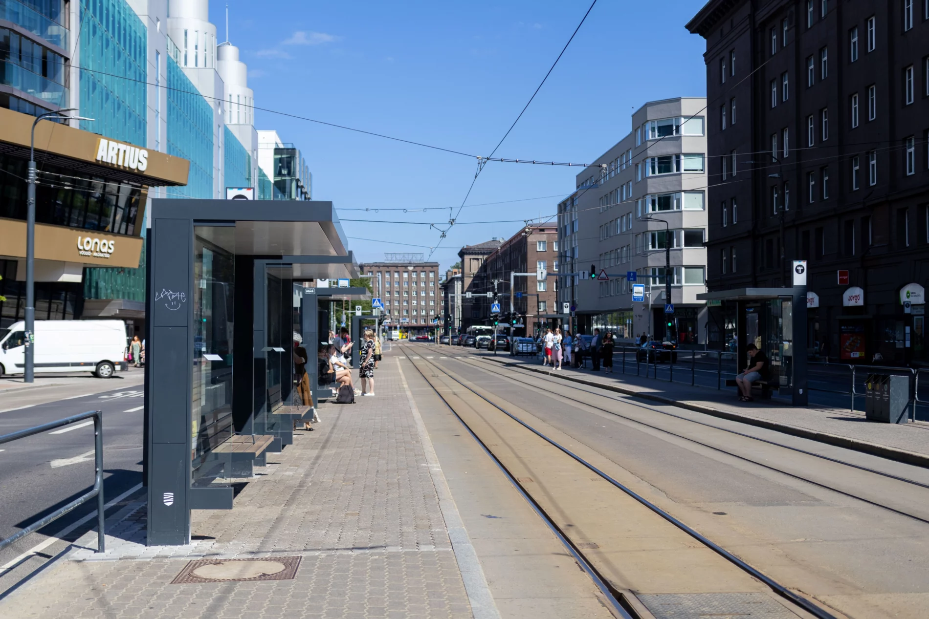 Inimesed ootavad päikeselise ilmaga trammipeatuses Tallinna kesklinnas, varju pakkuvat haljastust peatuse lähedal ei ole.