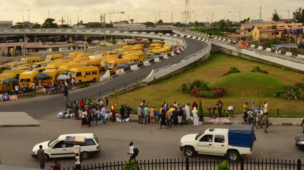 A drone view of the popular obalende section of lagos with rows of yellow 'danfo' buses under dark gold evening sky.