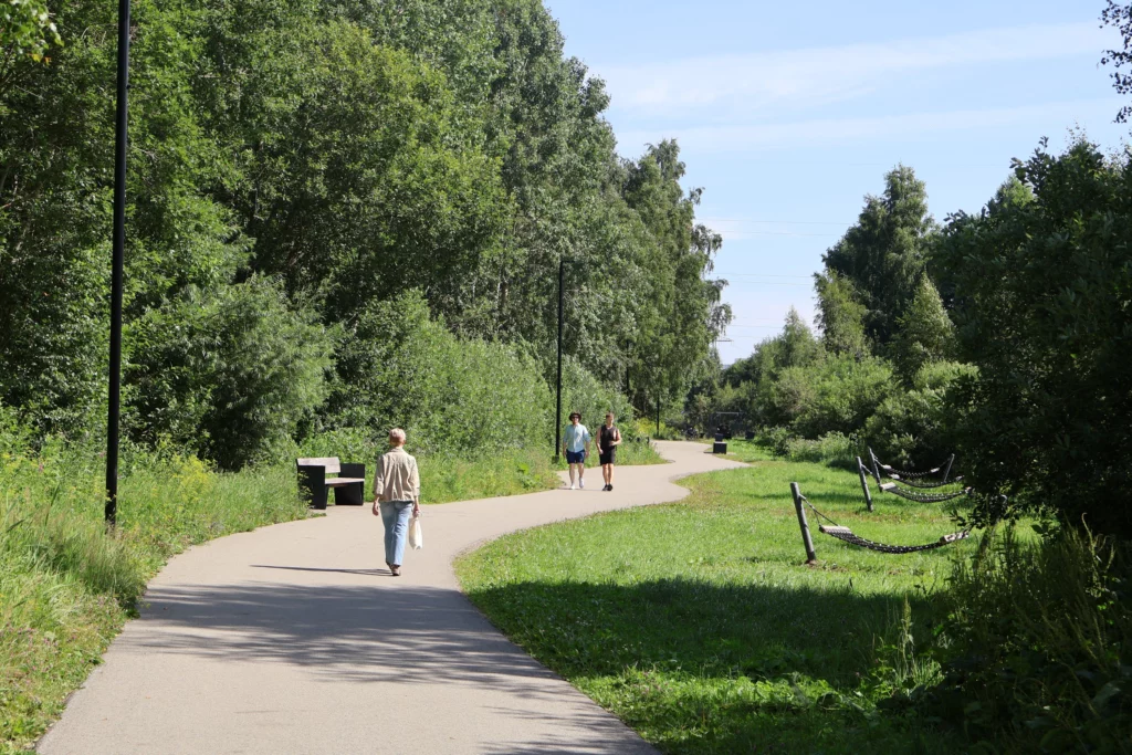 Inimesed jalutavad käänulisel jalakäijatele mõeldud asfaltrajal, mõlemal pool on kõrgete puudega mets,