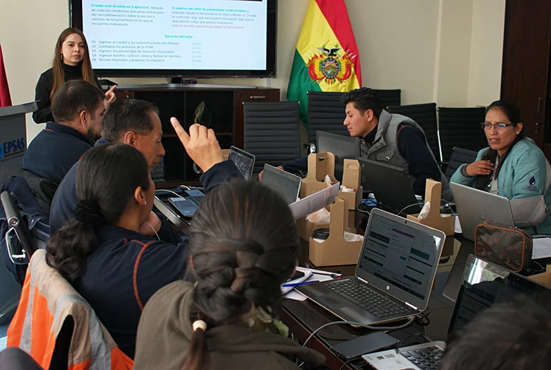 A workshop participant gestures towards a presentation screen as others follow the exercise on their laptops.