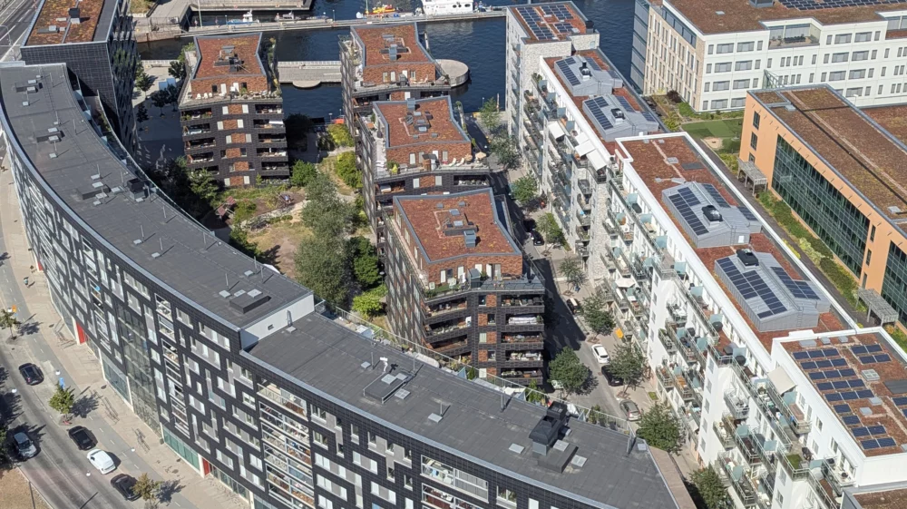 Arial view of roofs of apartment buildings with solar arrays and plants on the roofs.