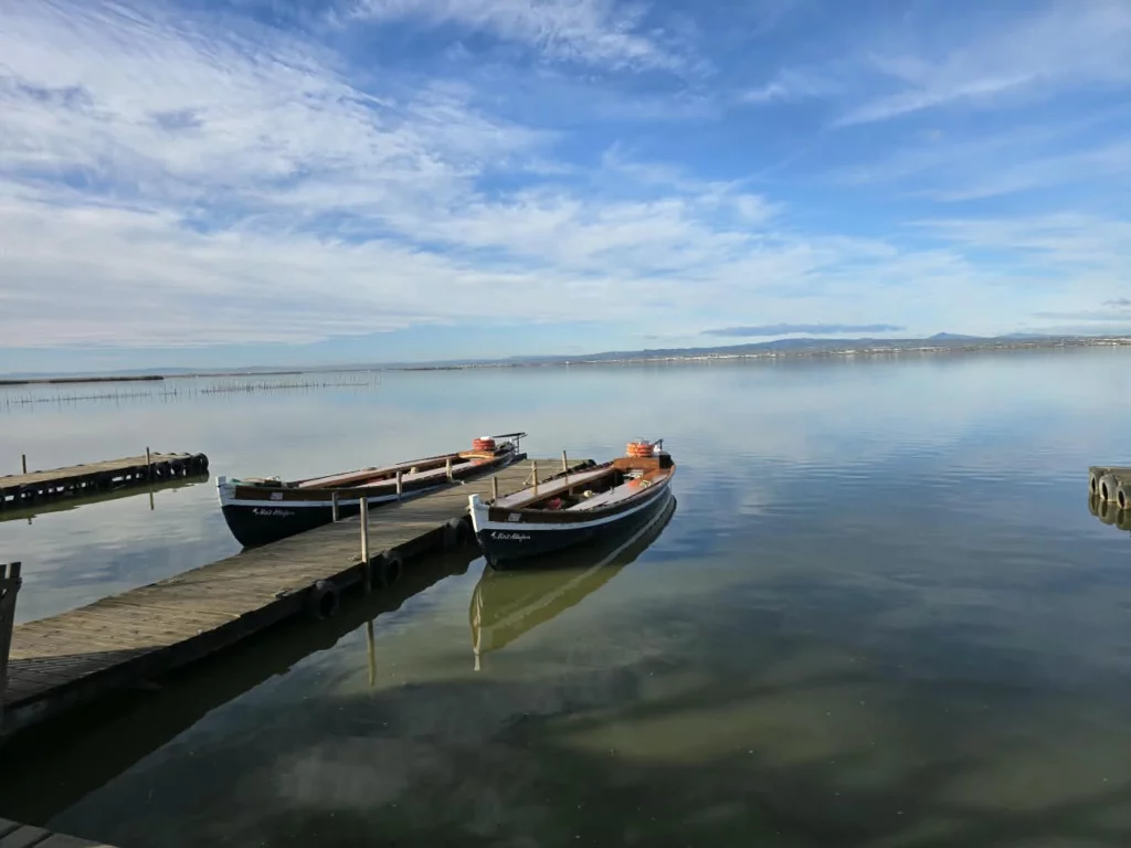 Two canoes are tied to a dock extending into placid waters beneath a blue, cloud-streaked sky