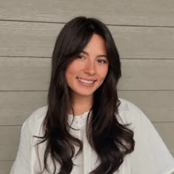 Ashley Ingalsbe smiles for the camera wearing a white short-sleeved blouse and her brown hair falls on her shoulders