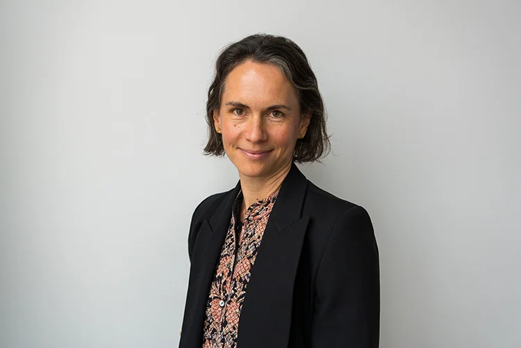 Marie Jürisoo, wearing a black blazer over a patterned blouse, against a plain light background.