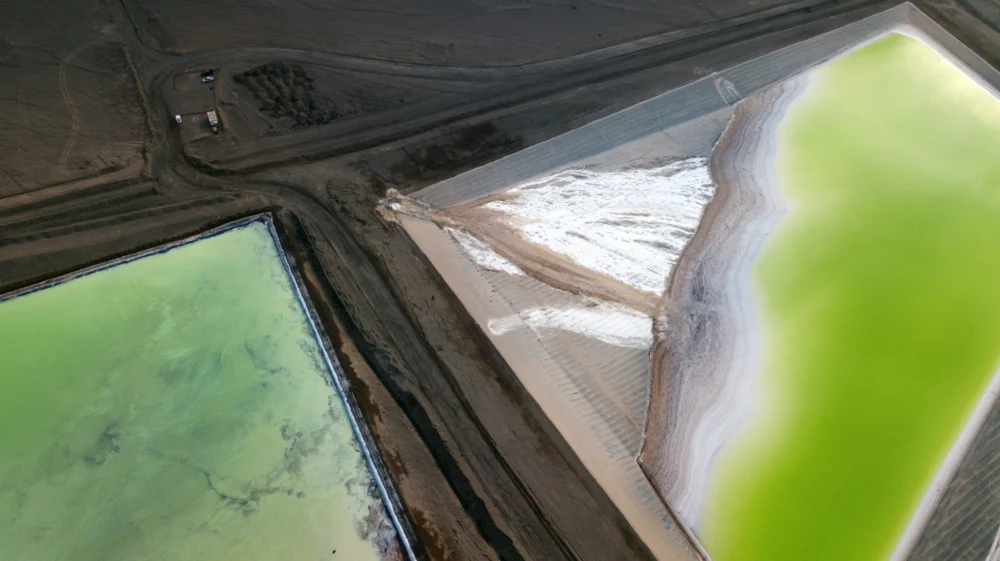 Aerial view of a lithium mine in Chile, showing dark brown earth surrounding fluorescent green brine pools.