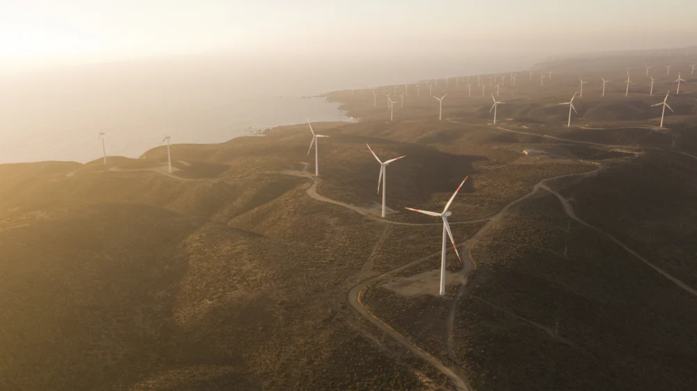 Aerial view of wind turbines dotting a rugged brown hillside along the coast in Chile at sunset.