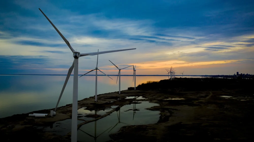 Wind turbines line the waterfront at sunset near Woodlawn Beach in upstate New York, in the Buffalo area. The sky is cloudy with dark blue and orange streaks.