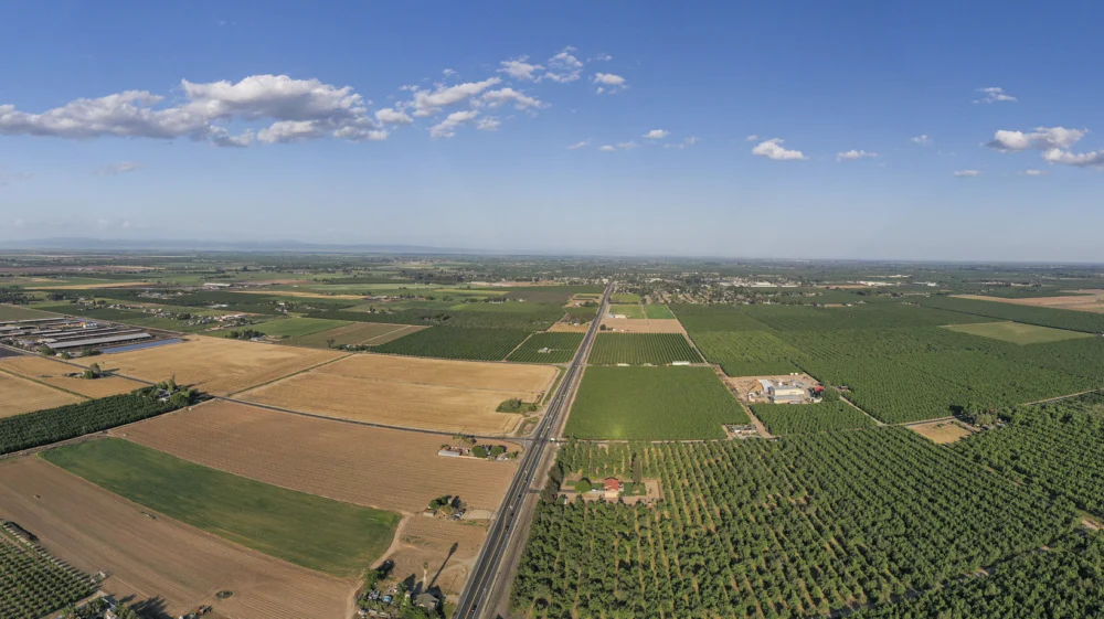 Aerial panoramic view of brown and green farmland beneath a blue, lightly clouded sky near Escalon, San Joaquin County, Central Valley, California