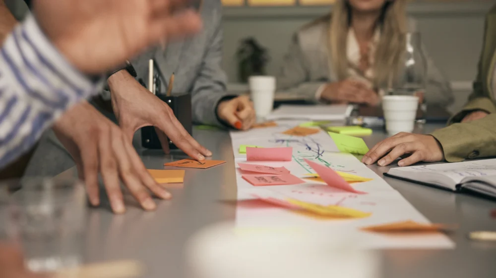 Adhesive notes stuck on paper at table with male and female coworkers in office meeting