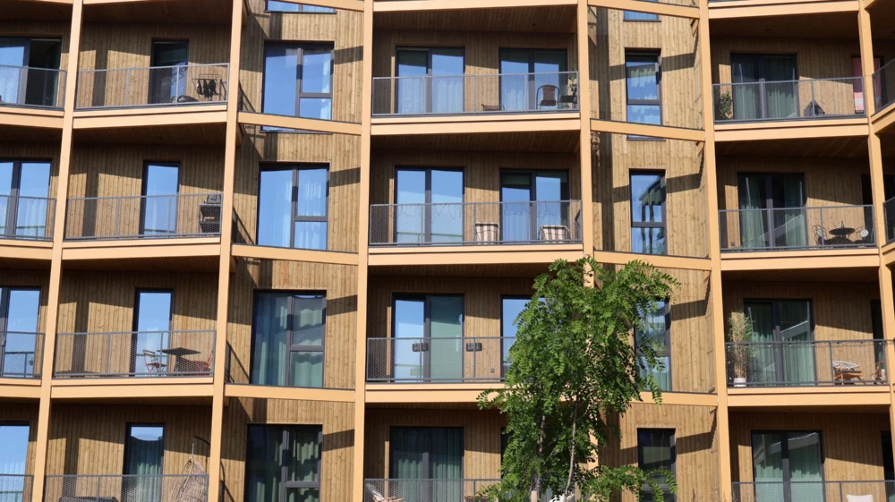 Modern timber-clad residential building with rows of balconies and a tree in the foreground